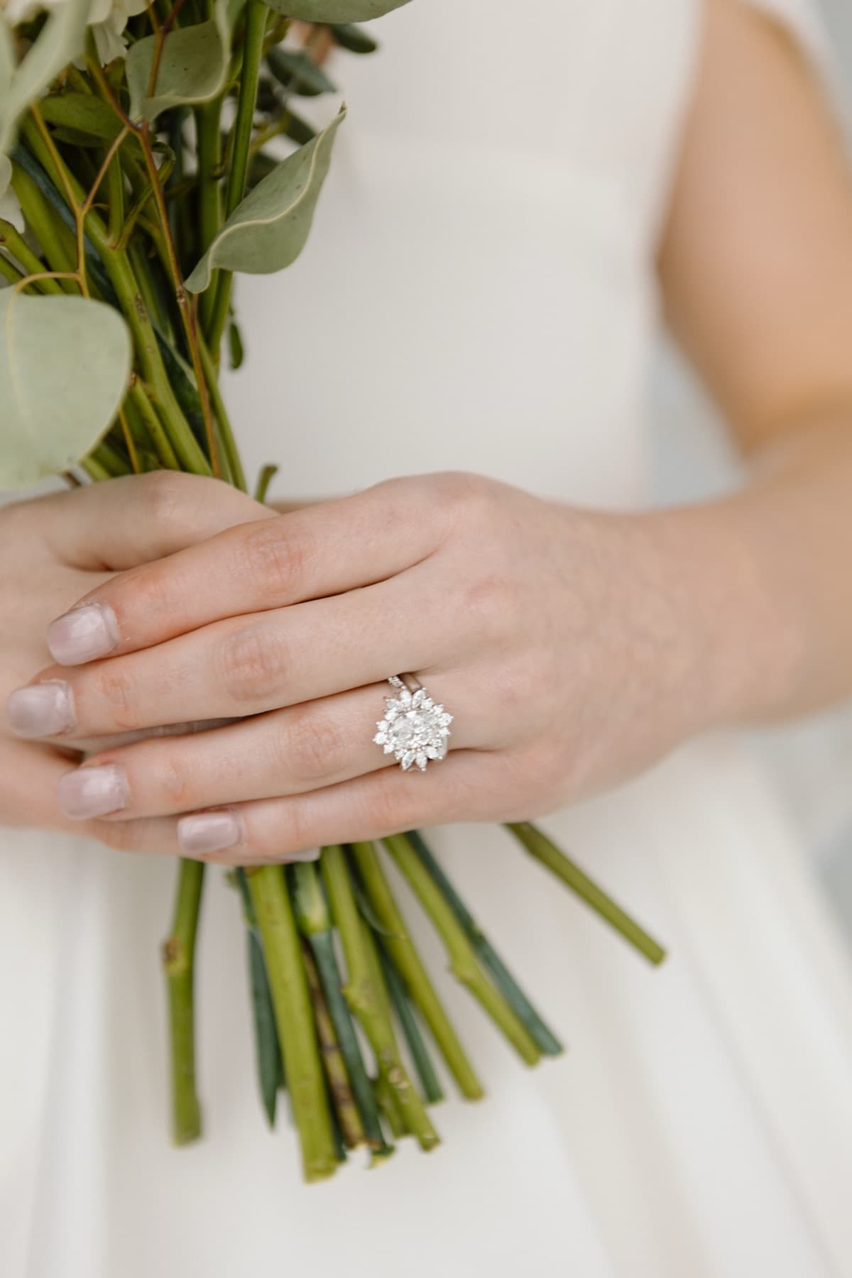 Halo diamond engagement ring on hand with bridal bouquet — custom ring from Gold & Diamond Company