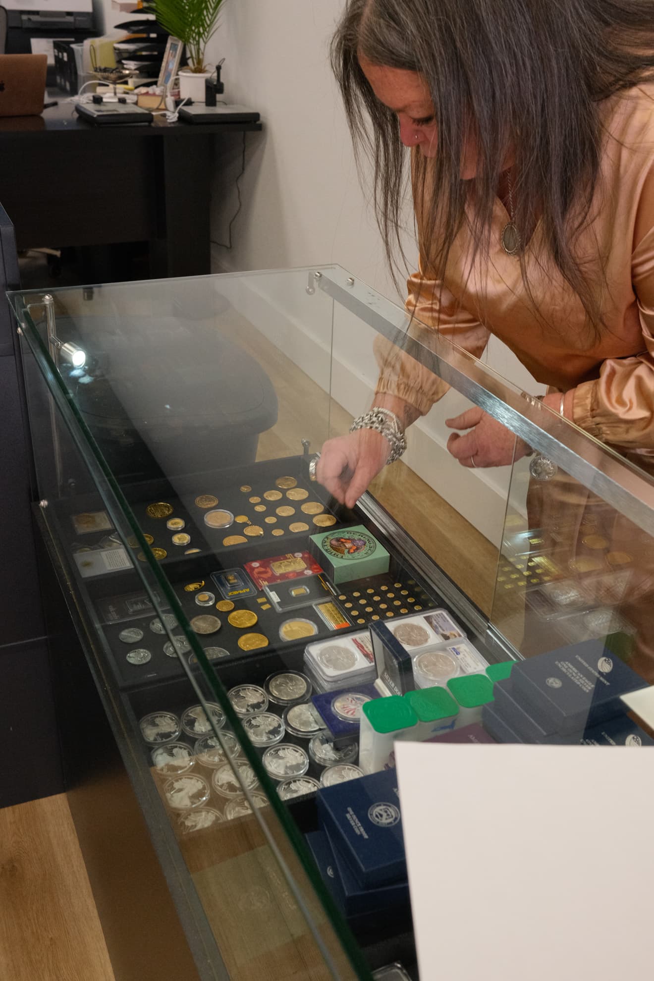 Staff examining gold and silver coins in a glass display case at Gold & Diamond Company showroom in Rogers, AR